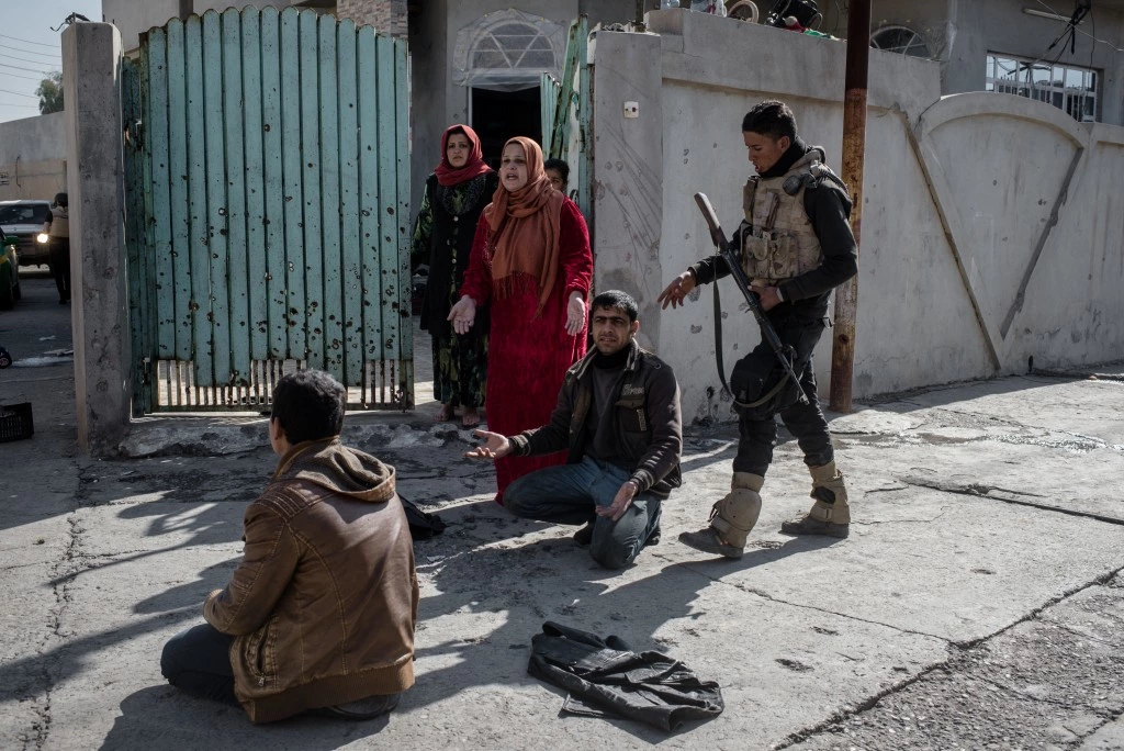 An officer with the Iraqi National Security Service (NSS) subdues civilians during a raid on suspected ISIS militants in eastern Mosul, Iraq on Feb. 21, 2017. The teenager facing away from the camera was arrested on suspected ISIS ties; the man on the right facing the camera was not arrested but was forced to the ground so he would not interfere.