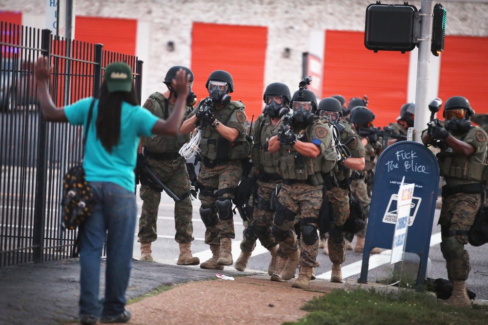 FERGUSON, MO - AUGUST 11:  (EDITORS NOTE: Image contains profanity) Police force protestors from the business district into nearby neighborhoods on August 11, 2014 in Ferguson, Missouri. Police responded with tear gas and rubber bullets as residents and their supporters protested the shooting by police of an unarmed black teenager named Michael Brown who was killed Saturday in this suburban St. Louis community. Yesterday 32 arrests were made after protests turned into rioting and looting in Ferguson.  (Photo by Scott Olson/Getty Images)