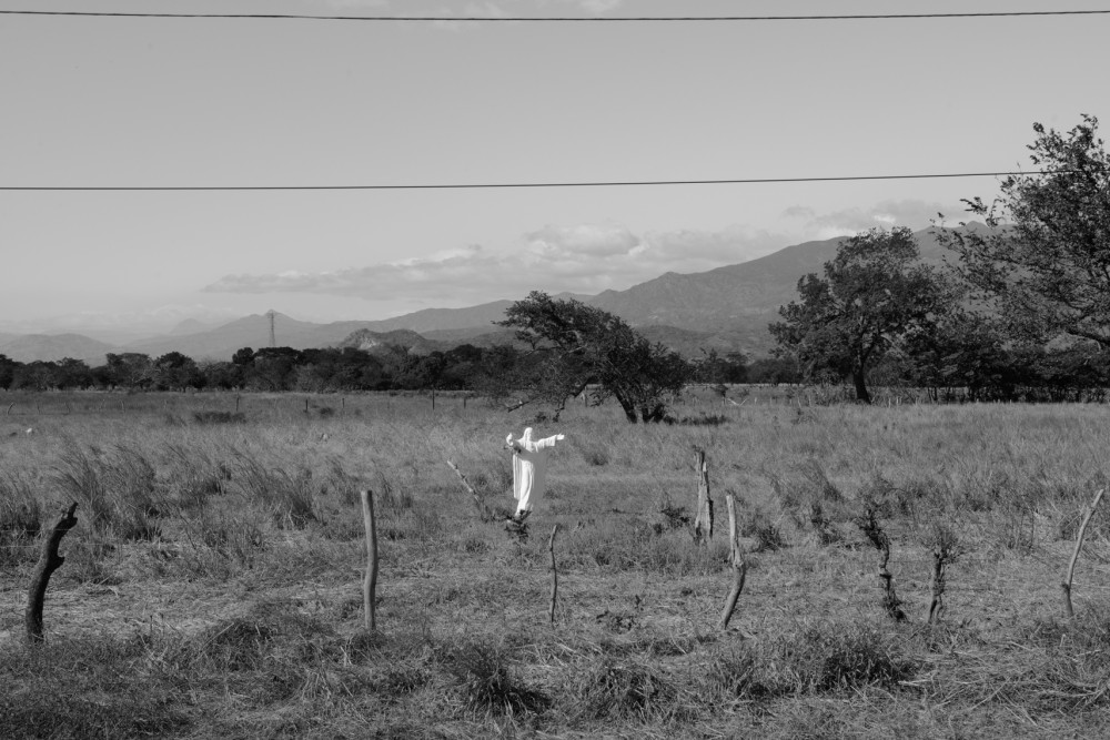 A roadside statue of Jesus in front of a trail used by migrants by the side of a highway.