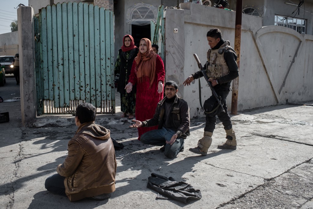 An officer with the Iraqi National Security Service (NSS) subdues civilians during a raid on suspected ISIS militants in eastern Mosul, Iraq on Feb. 21, 2017. The teenager facing away from the camera was arrested on suspected ISIS ties; the man on the right facing the camera was not arrested but was forced to the ground so he would not interfere.