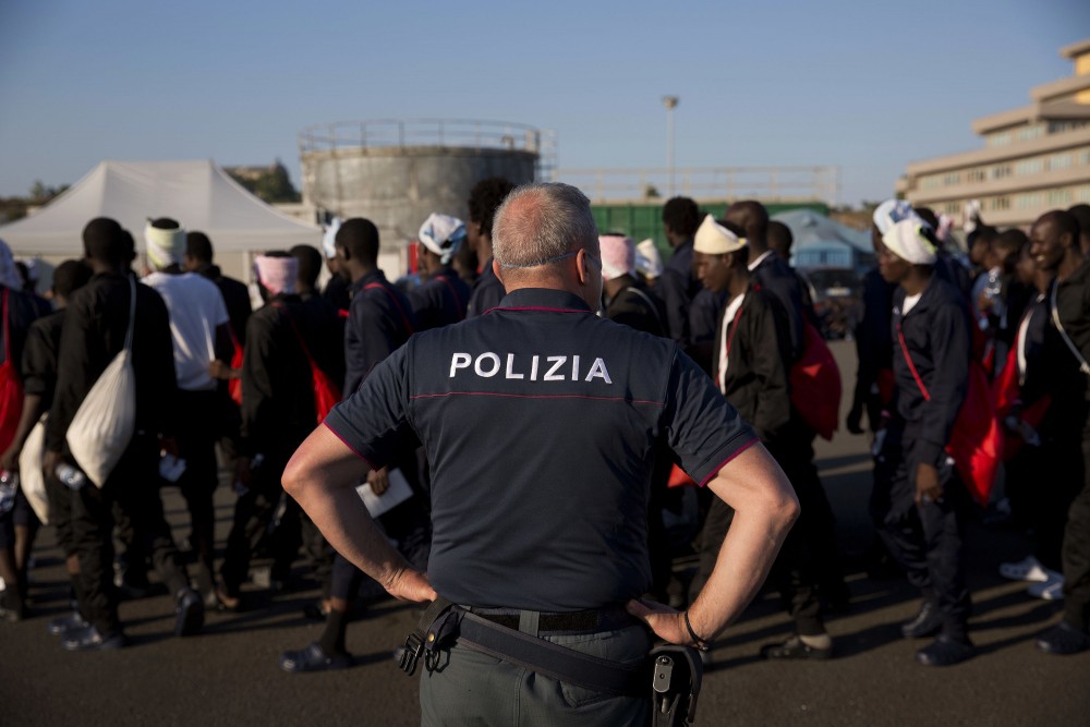 An Italian border police officer escorts sub Saharan men on their way to a relocation center, after arriving in the Golfo Azzurro rescue vessel at the port of Augusta, in Sicily, Italy, with hundreds of migrants aboard, rescued by members of Proactive Open Arms NGO, on Friday, June 23, 2017. (AP Photo/Emilio Morenatti)