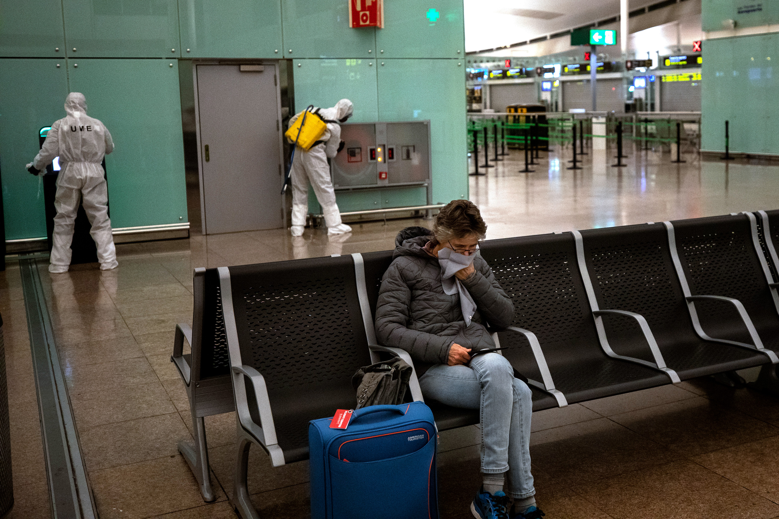 Uma mulher cobre a boca enquanto soldados da Unidade Militar de Emergências da Espanha desinfetam o terminal do aeroporto de Barcelona em 19 de março de 2020.
